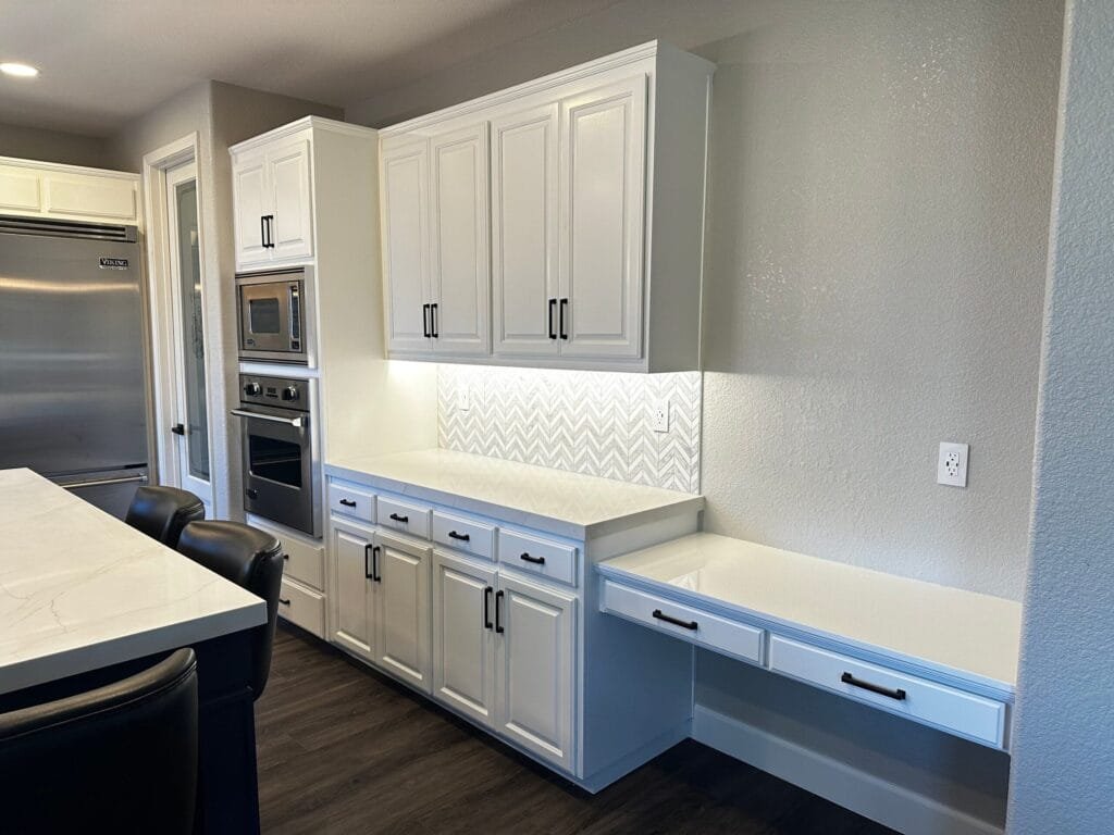 Kitchen Remodeling Services in Blackhawk, CA 2 Modern kitchen with white cabinets, a built-in desk area, stainless steel appliances, and a marble countertop island. Herringbone backsplash is illuminated under the cabinets—perfect inspiration for your next home renovation.