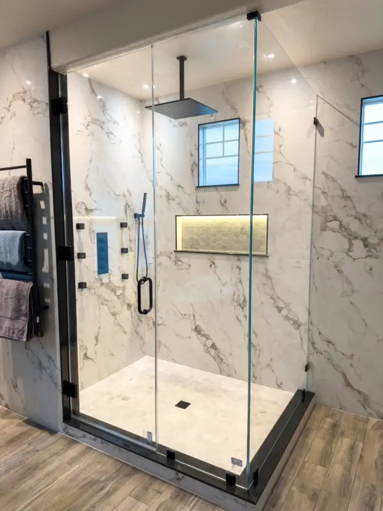 Modern walk-in shower with glass doors, marble-patterned walls, rainfall showerhead, and built-in shelf with lighting—perfect for a stylish bath remodel or home renovation. Towels hang on a rack just outside for convenience.